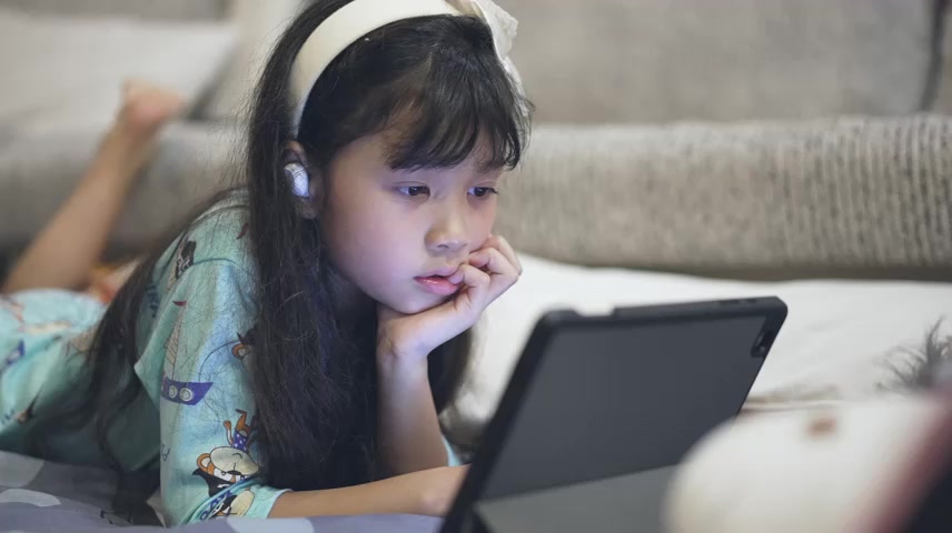 小女孩晚上在卧室玩数字平板电脑在线学习.